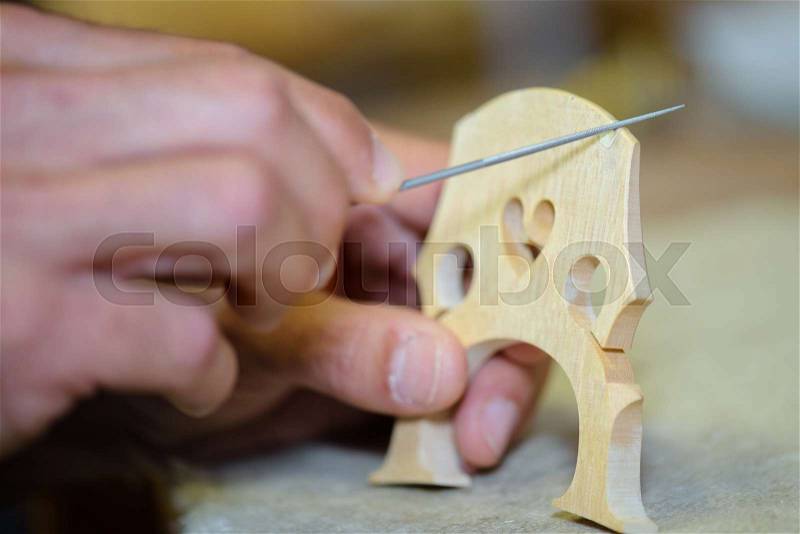 Closeup of craftsman making musical instrument bridge, stock photo