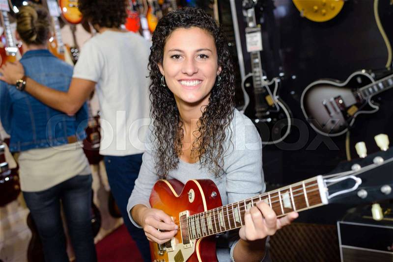 Young woman testing guitar in shop, stock photo