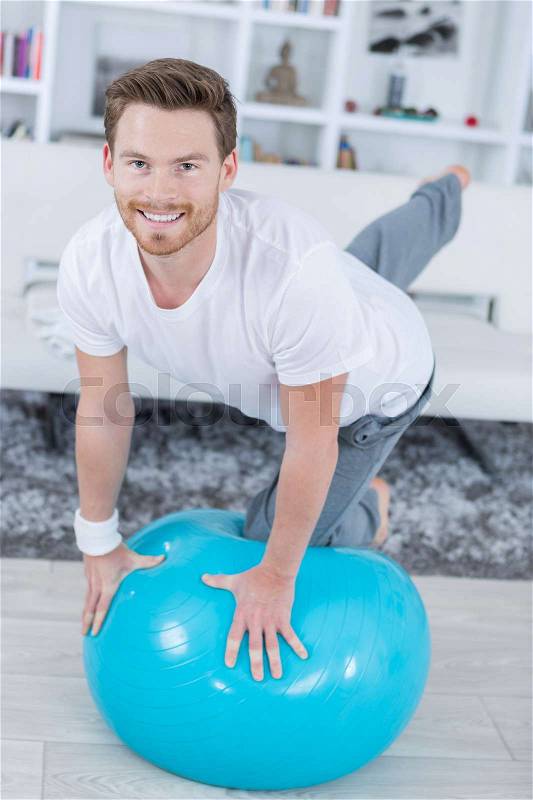 Attractive young man with swiss ball doing exercises at home, stock photo