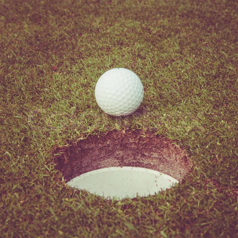 Golf ball on lip of cup. Golf ball on green grass in golf course. Vintage, retro style, stock photo