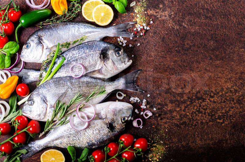 Fresh uncooked fish, dorado, sea bream with lemon, herbs, vegetables and spices on rustic background. Top view, stock photo