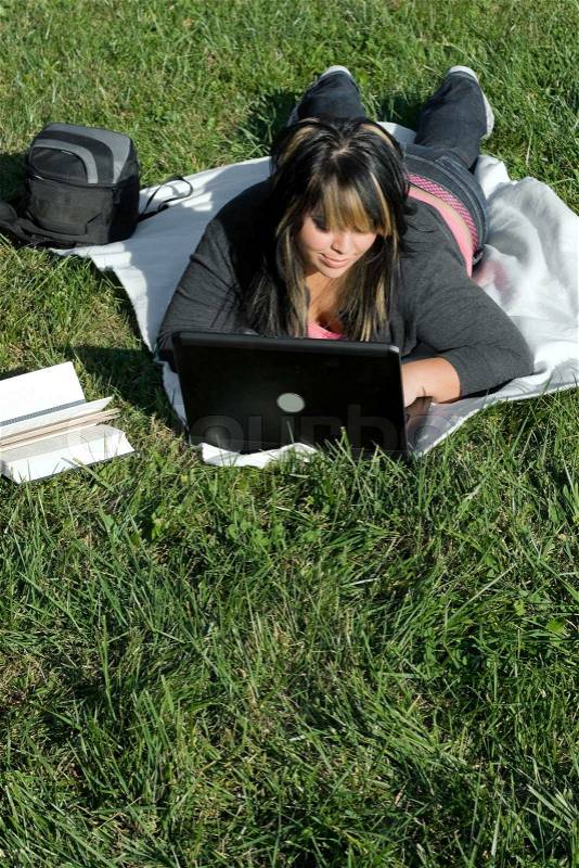A young student using her laptop computer while laying in the grass on a nice day, stock photo