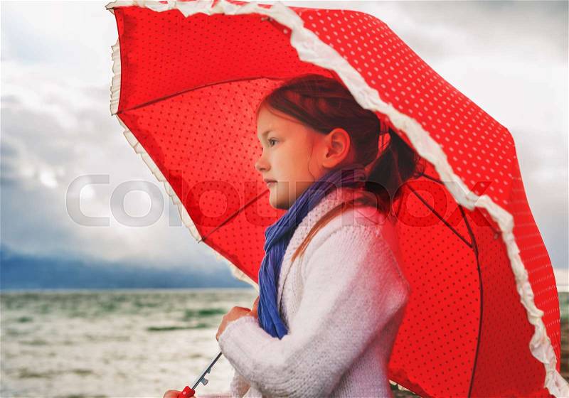 Little girl with big red umbrella next to lake on a very cold day, stock photo