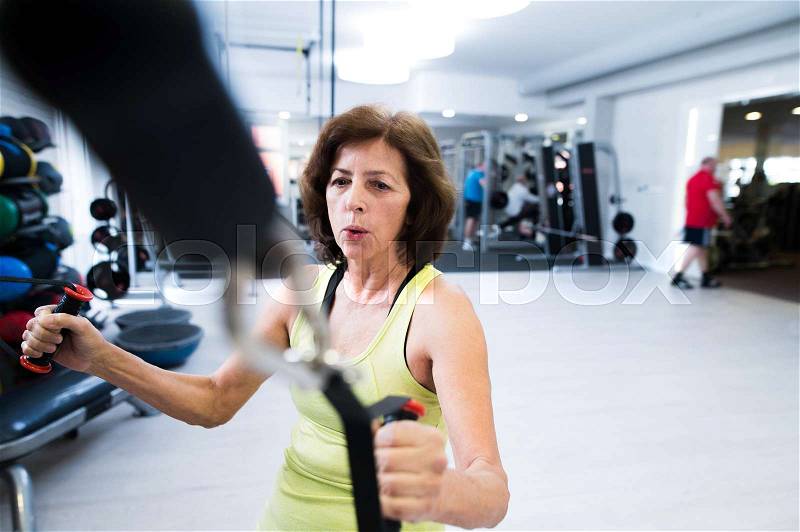 Beautiful fit senior woman in sports clothing in gym working out with resistance bands, stock photo