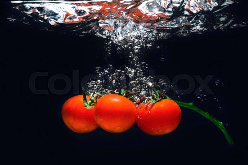 Fresh red tomatoes in splash of water isolated on black background, stock photo