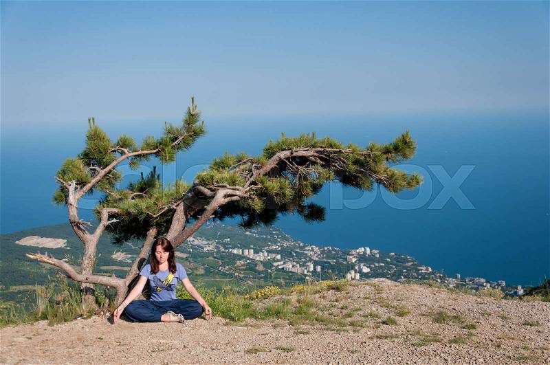 Young woman meditating in lotus position while doing yoga under the tree on the top of the mountain. Travel, Healthy Lifestyle concept, stock photo