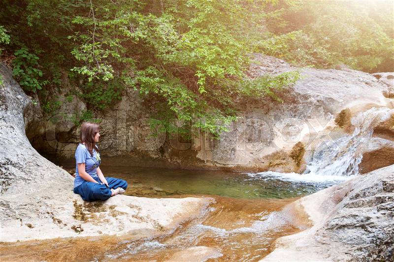 Young woman meditating in lotus position while doing yoga in a wonderful forest near waterfall. Travel, Healthy Lifestyle concept, stock photo