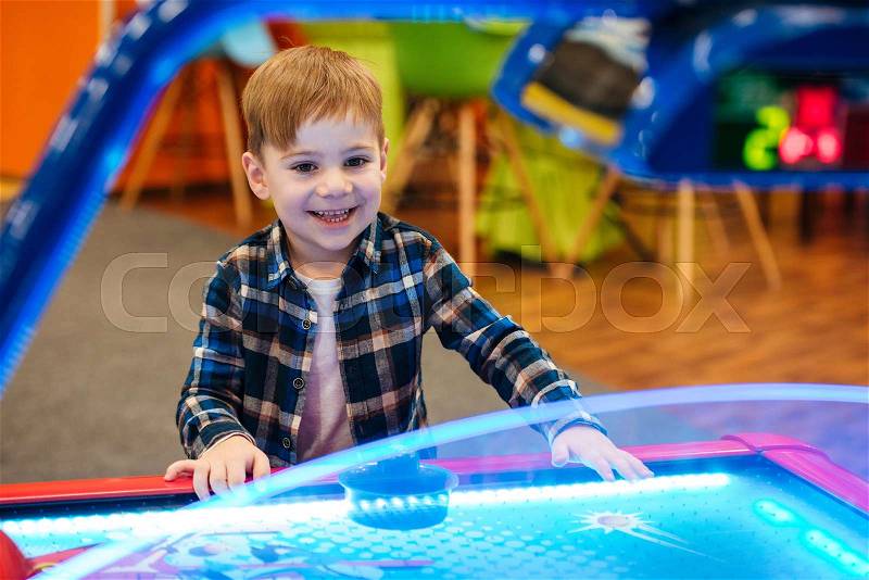 Happy little boy playing air hockey at indoor playground, stock photo