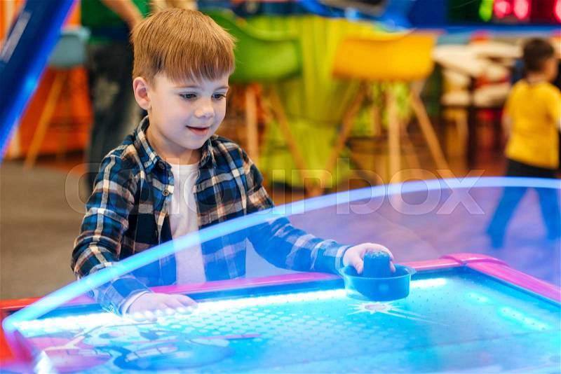 Cute little boy standing and playing air hockey at indoor amusement park, stock photo