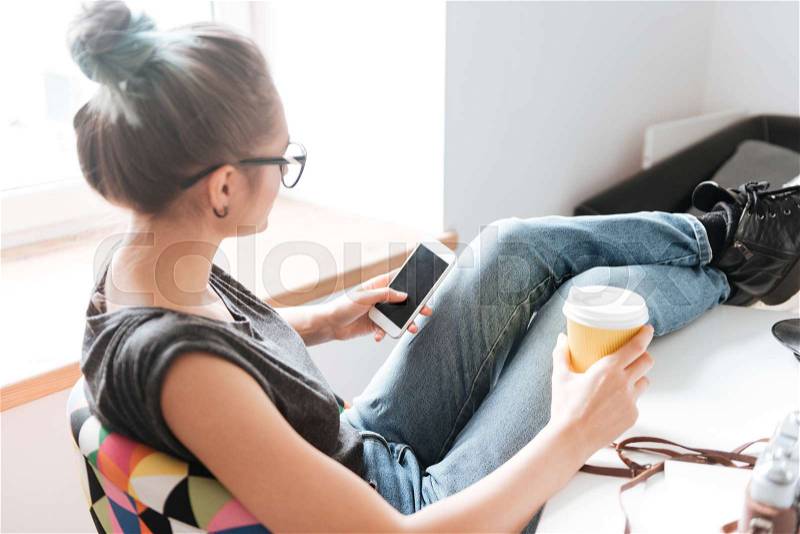 Back view of woman drinking coffee and using cell phone, stock photo