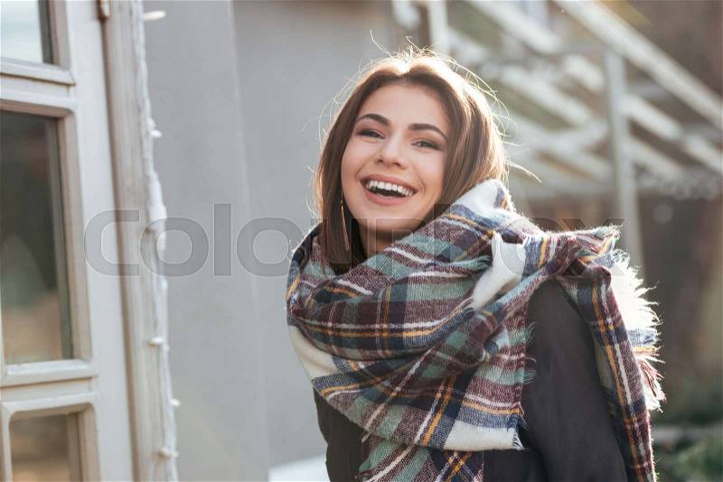 Image of young laughing lady looking at camera while walking near cafe outdoors, stock photo