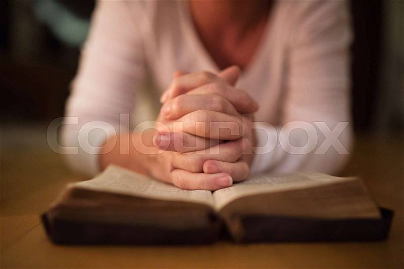 Unrecognizable woman praying with hands clasped together on her Bible. Close up, stock photo