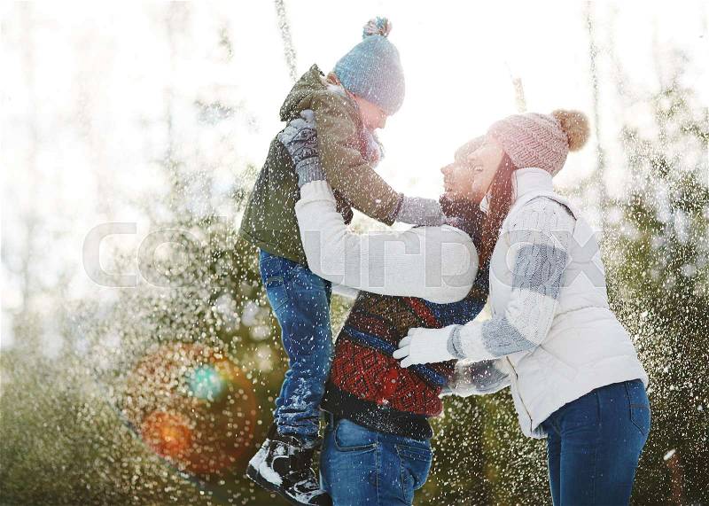 Laughing family of three playing in snowfall, stock photo