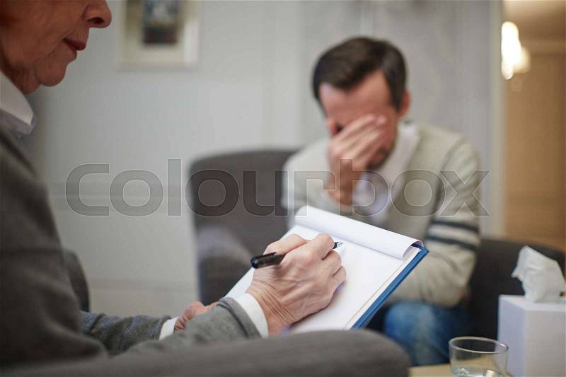 Psychologist making notes while patient telling his story, stock photo