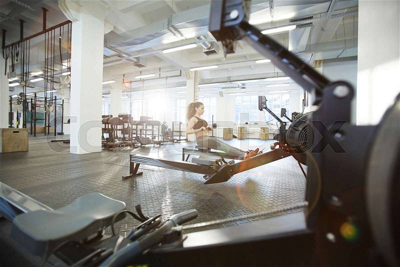 Young woman exercising on rowing machine in gym, stock photo