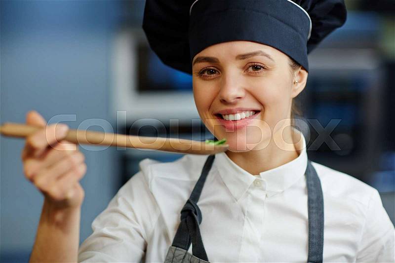 Attractive woman in chef cap tasting food during preparation, stock photo