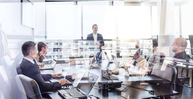 Successful team leader and business owner leading informal in-house business meeting. Business people working on laptops in foreground and glass reflections. Business and entrepreneurship concept, stock photo
