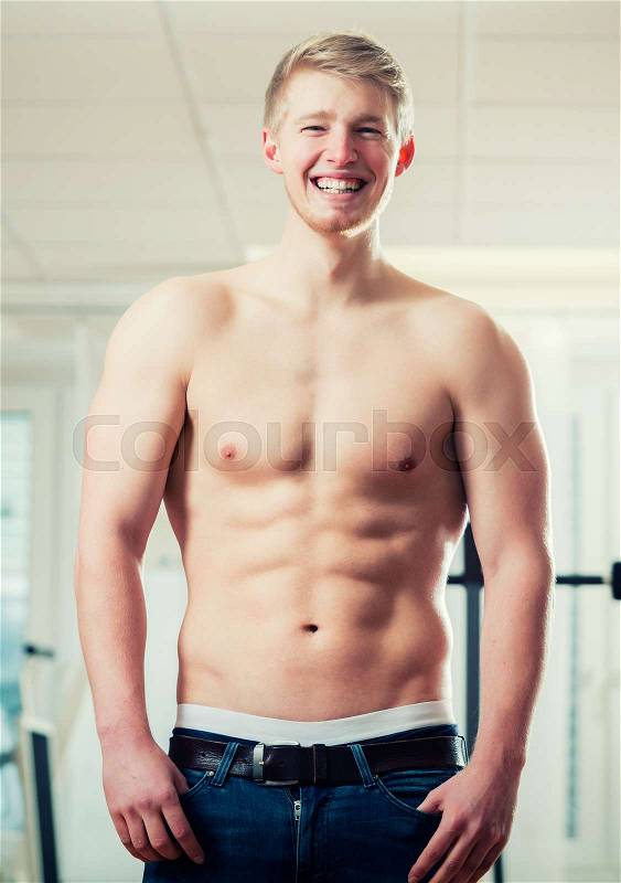 Trained athlete showing his muscles and six pack in health club gym, stock photo