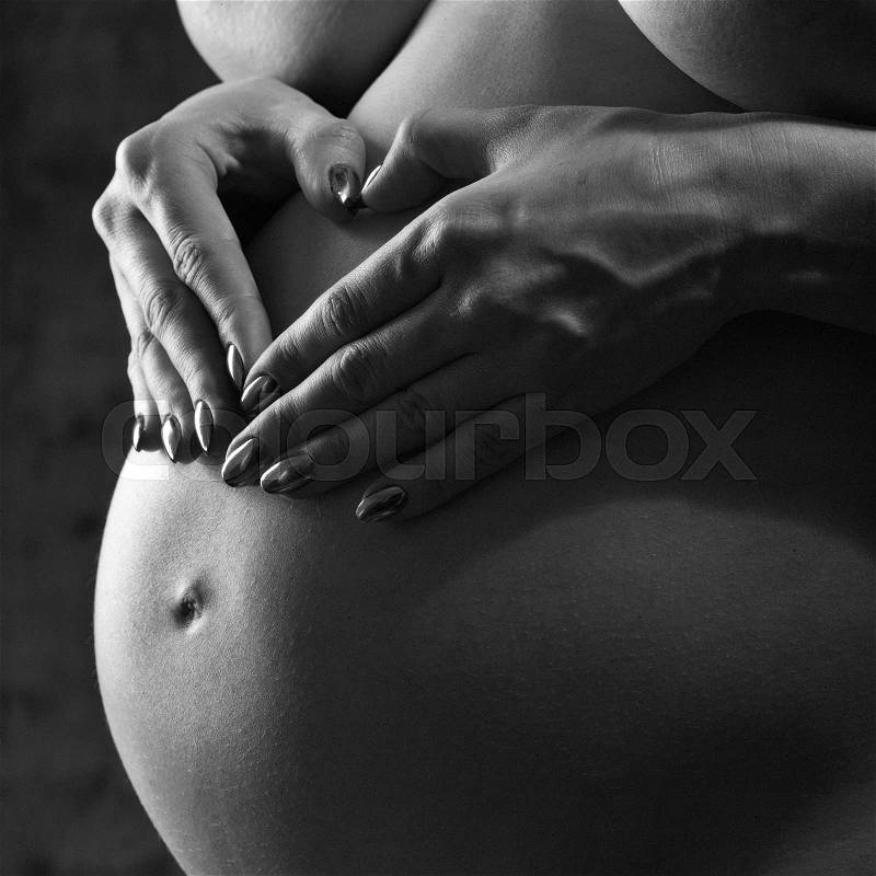 Pregnant woman making love sign over his stomach. Studio black and white female portrait, stock photo