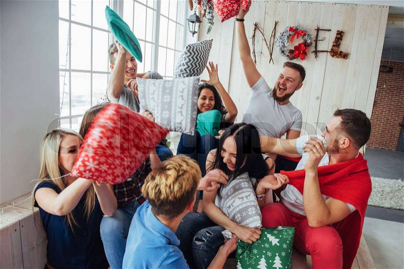 Crazy young best friends fighting pillows at home. Mixed race group of people. Concept of entertainment and lifestyle, stock photo