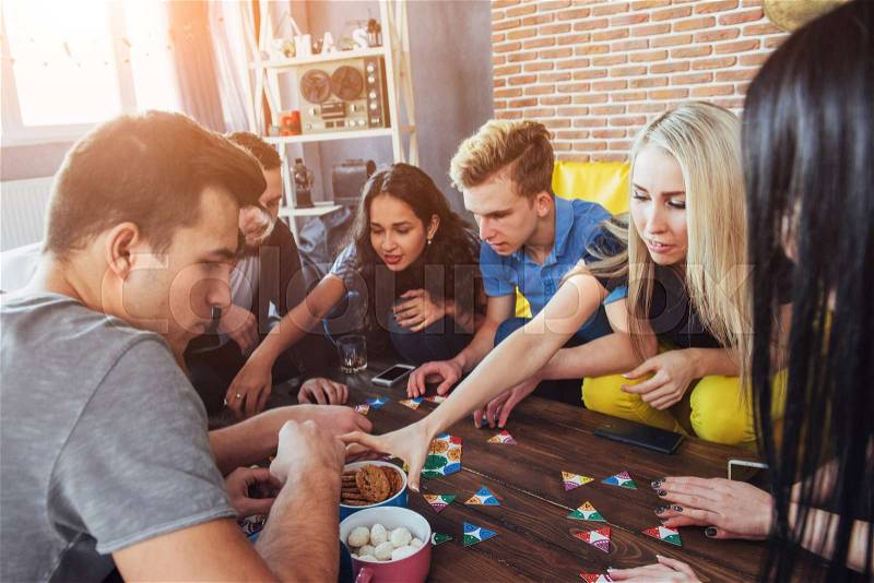 Group of creative friends sitting at wooden table. People having fun while playing board game, stock photo