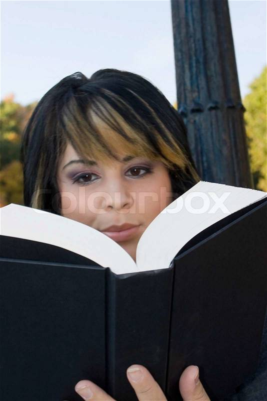 A young woman with highlighted hair reading a book or doing homework on campus, stock photo