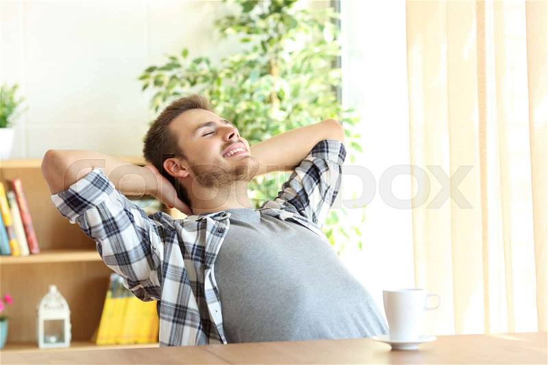 Portrait of a satisfied man relaxing with the arms in the head sitting on a chair at home with a warm light from a window, stock photo
