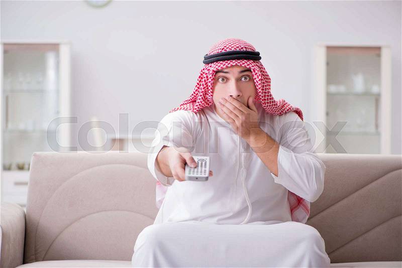 Young arab man watching tv sitting on the sofa, stock photo