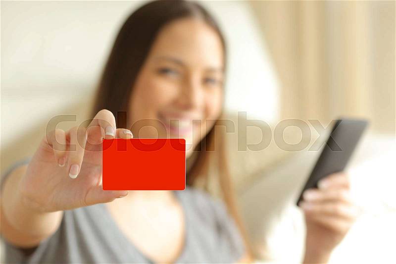 On line buyer holding a smart phone is showing a blank credit card and looking at camera, stock photo