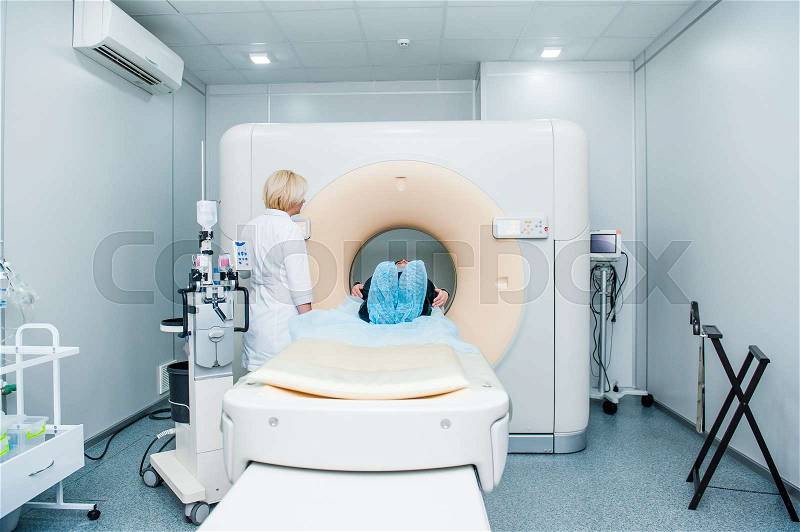 Female doctor adjusts computed tomography or computed axial tomography scan machine with lying patient in hospital room, stock photo