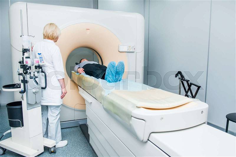 Female doctor adjusts computed tomography or computed axial tomography scan machine with lying patient in hospital room, stock photo
