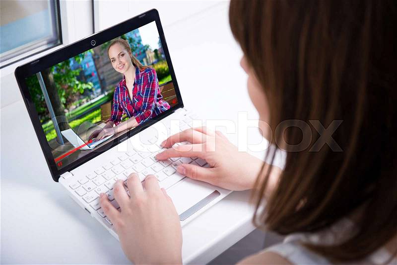Video blog concept - back view of young woman watching business video on laptop at home, stock photo