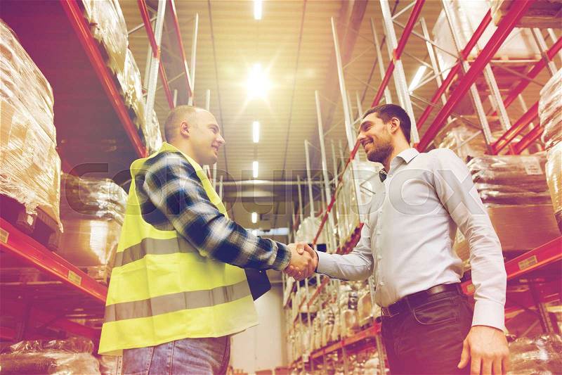 Wholesale, logistic, people and export concept - manual worker and businessmen with clipboard shaking hands and making deal at warehouse, stock photo