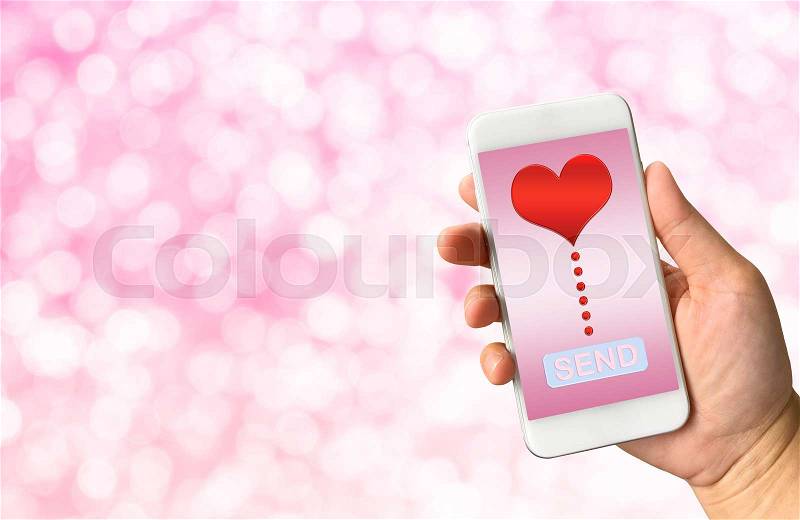 Hand holding smart phone on white pink bokeh background with word send and red heart for Valentine\'s Day, stock photo
