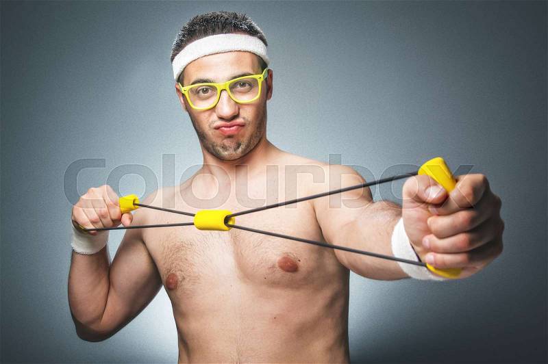 Funny man exercising over dark gray background. Nerd guy with eyeglasses holding expander. Close up of silly young man doing aerobics. Studio shot, stock photo