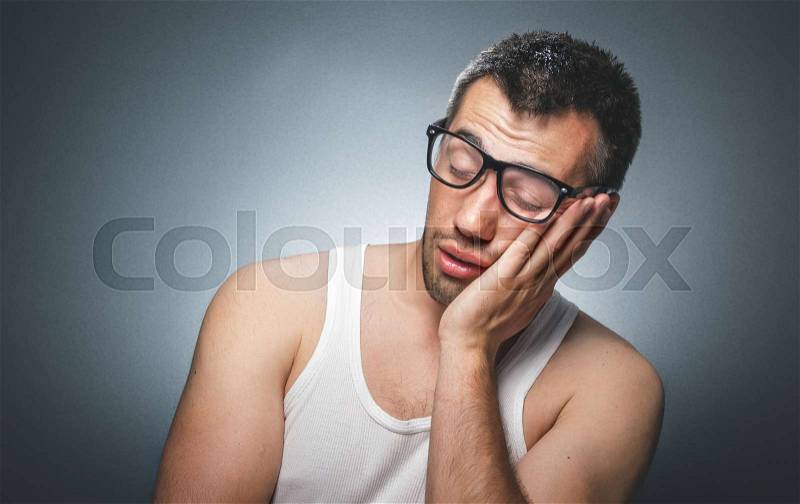 Sleepy young man wearing white undershirt. Funny guy yawn, comic facial exspression over gray dark background, stock photo