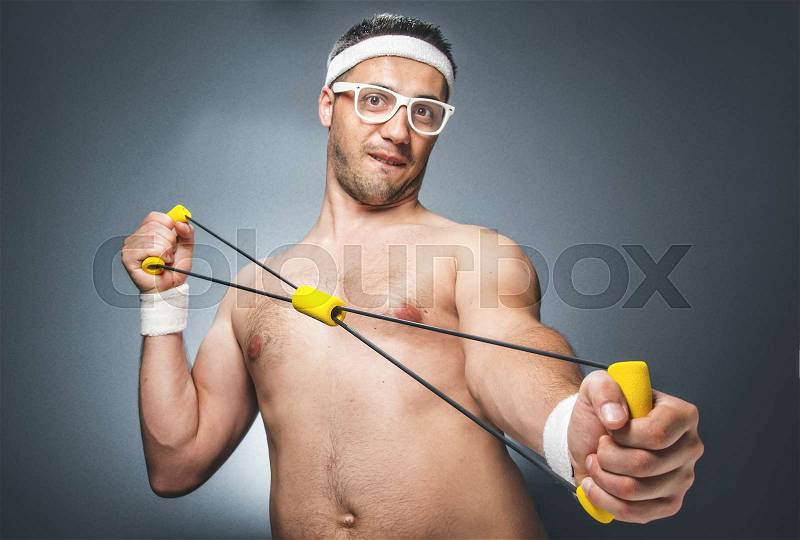 Funny man exercising over dark gray background. Nerd guy with eyeglasses holding expander. Close up of silly young man doing aerobics. Studio shot, stock photo