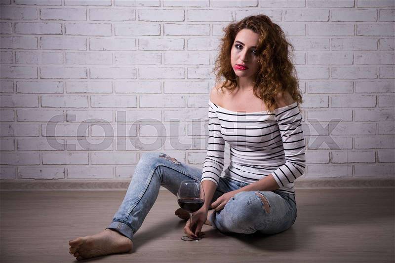 Female alcoholism - sad young beautiful woman sitting on the floor with glass of wine, stock photo