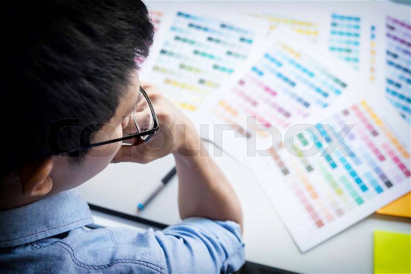 Top view of a young graphic designer working on a desktop computer and using some color swatches, top view, stock photo