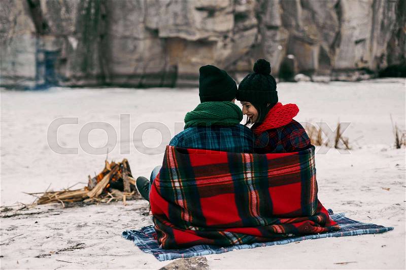Couple sitting near a bonefire. They are covered with a warm blanket because the is cold, stock photo