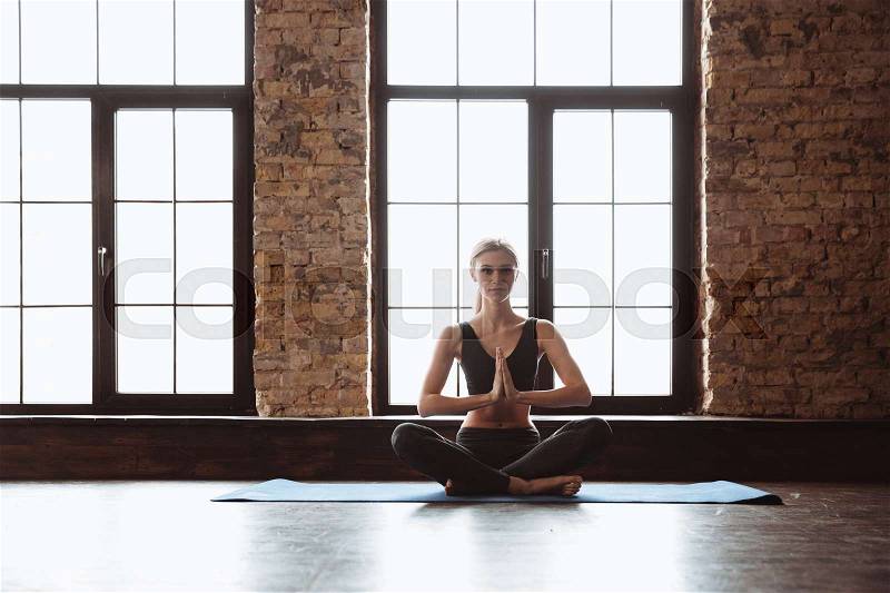 Picture of pretty young fitness lady sitting in gym near window while make yoga exercises, stock photo