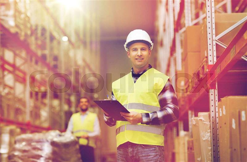 Wholesale, logistic, people and export concept - man with clipboard in reflective safety vest at warehouse, stock photo