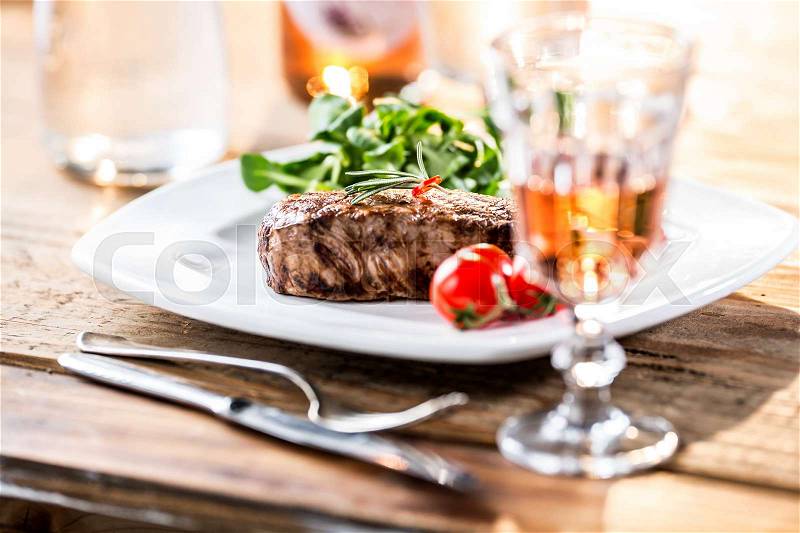 Beef Steak. Juicy beef steak. Gourmet steak with vegetables and glass of rose wine on wooden table, stock photo