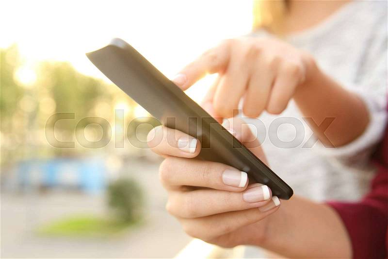 Close up of a friend hands using a smart phone together outdoors at sunset with a park in the background, stock photo