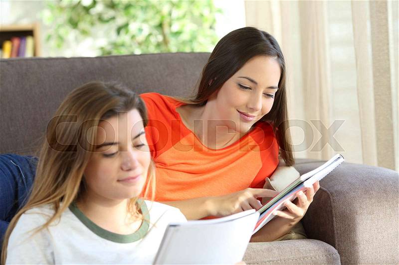 Two concentrated students learning reading notebooks on a couch in the living room at home, stock photo