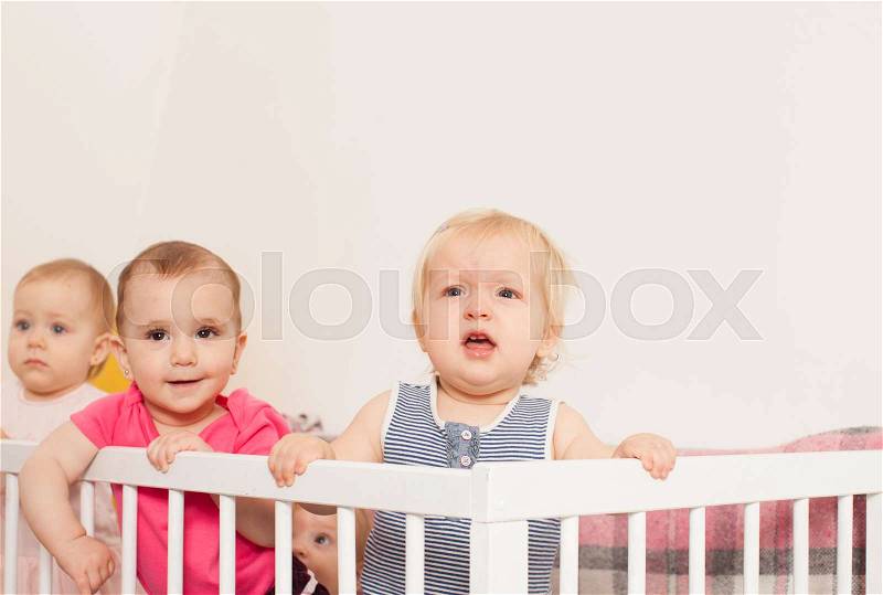 Three cute little baby girls are stand up in the crib, stock photo