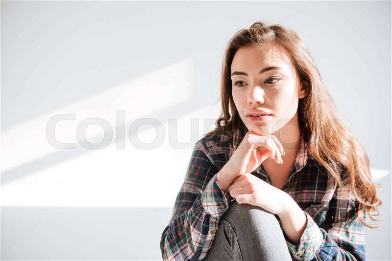 Picture of young woman sitting on floor at studio over white background and posing, stock photo