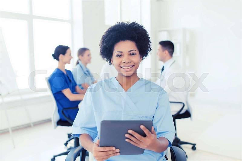 Clinic, profession, people and medicine concept - happy african american female doctor or nurse with tablet pc computer over group of medics meeting at hospital, stock photo