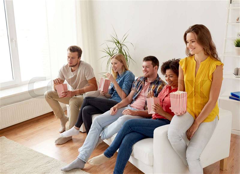 Friendship, leisure, junk food, people and entertainment concept - happy friends eating popcorn and watching tv at home, stock photo