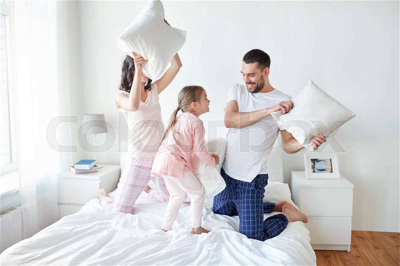 People, family and morning concept - happy child with parents having pillow fight in bed at home, stock photo